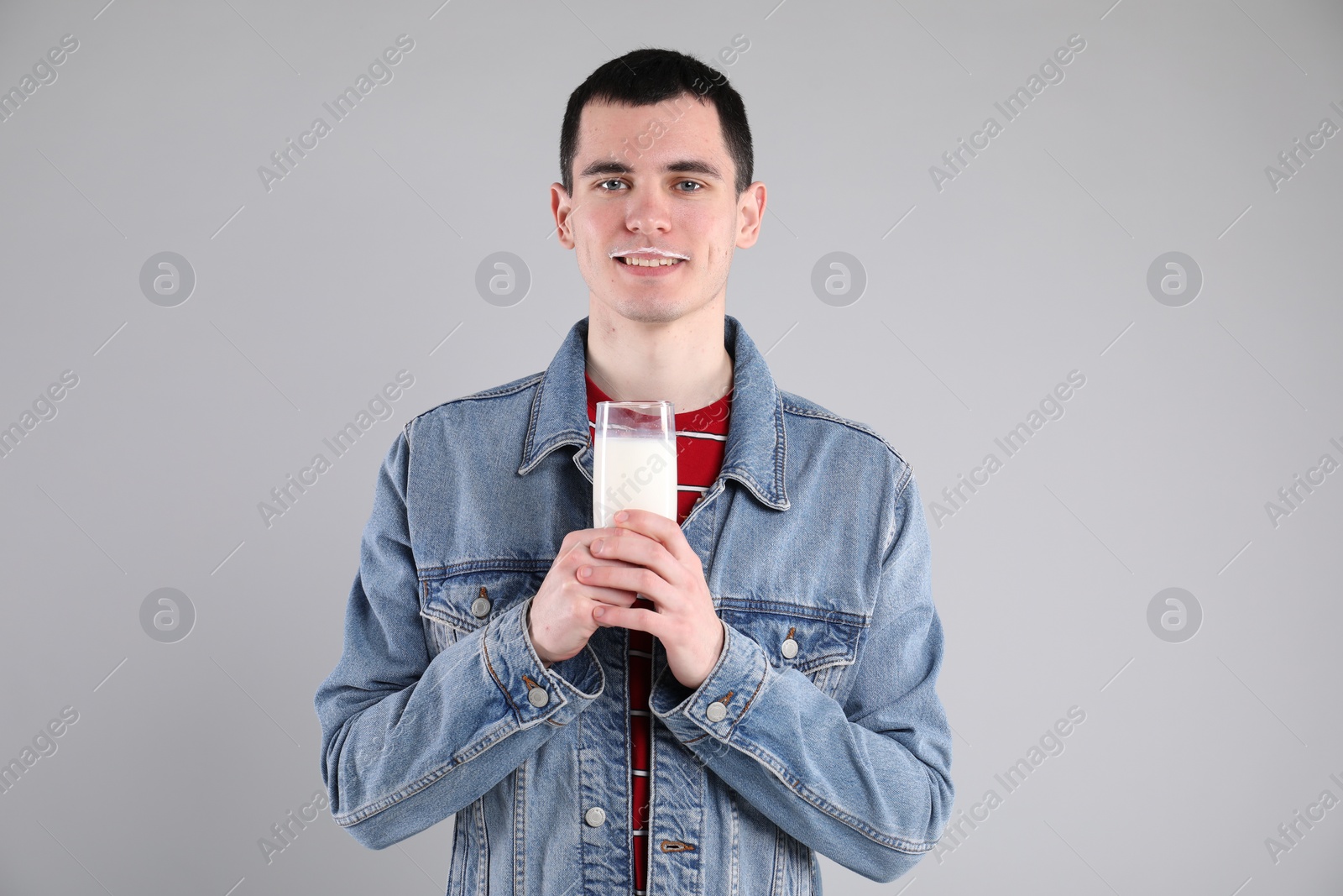 Photo of Happy man with milk mustache holding glass of tasty dairy drink on gray background