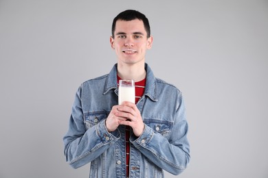 Happy man with milk mustache holding glass of tasty dairy drink on gray background