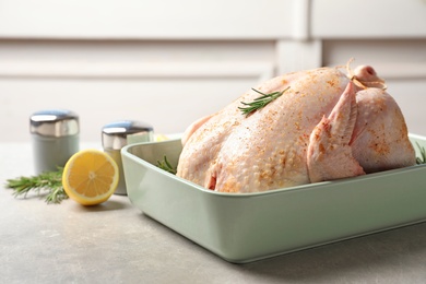 Photo of Baking dish with raw spiced turkey and rosemary on table. Space for text
