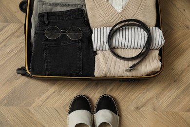 Photo of Open suitcase with folded clothes, accessories and shoes on floor, flat lay