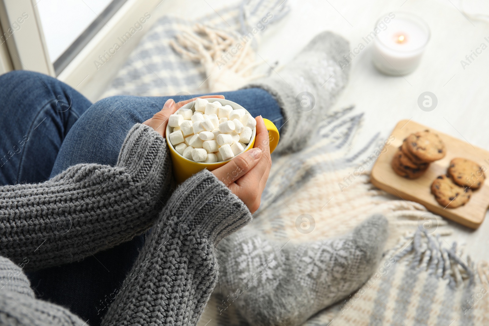 Photo of Woman with cup of hot cocoa sitting on window sill, closeup. Winter drink