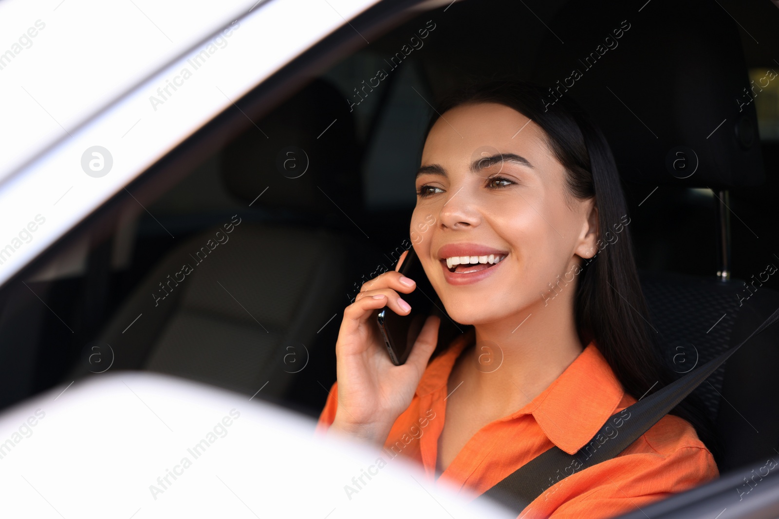 Photo of Happy young woman talking on smartphone in modern car, view from outside