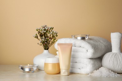 Photo of Composition with different spa products, candles and flowers on beige table. Space for text