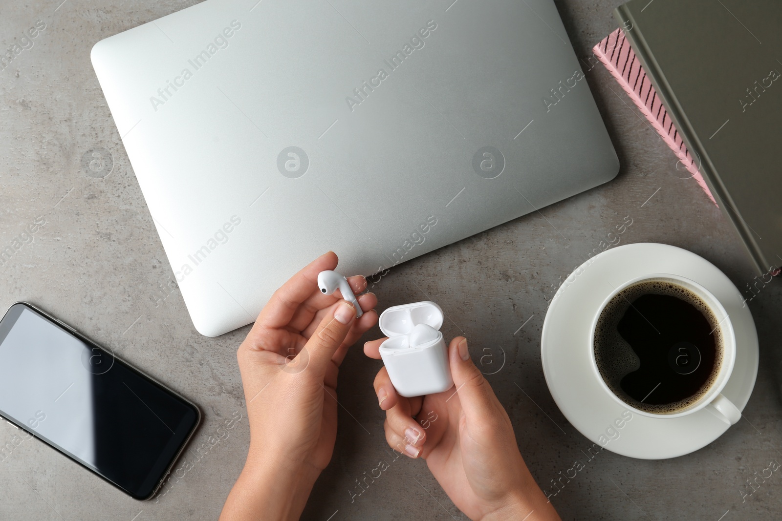 Photo of Woman putting wireless earphones in charging case at grey stone table, top view