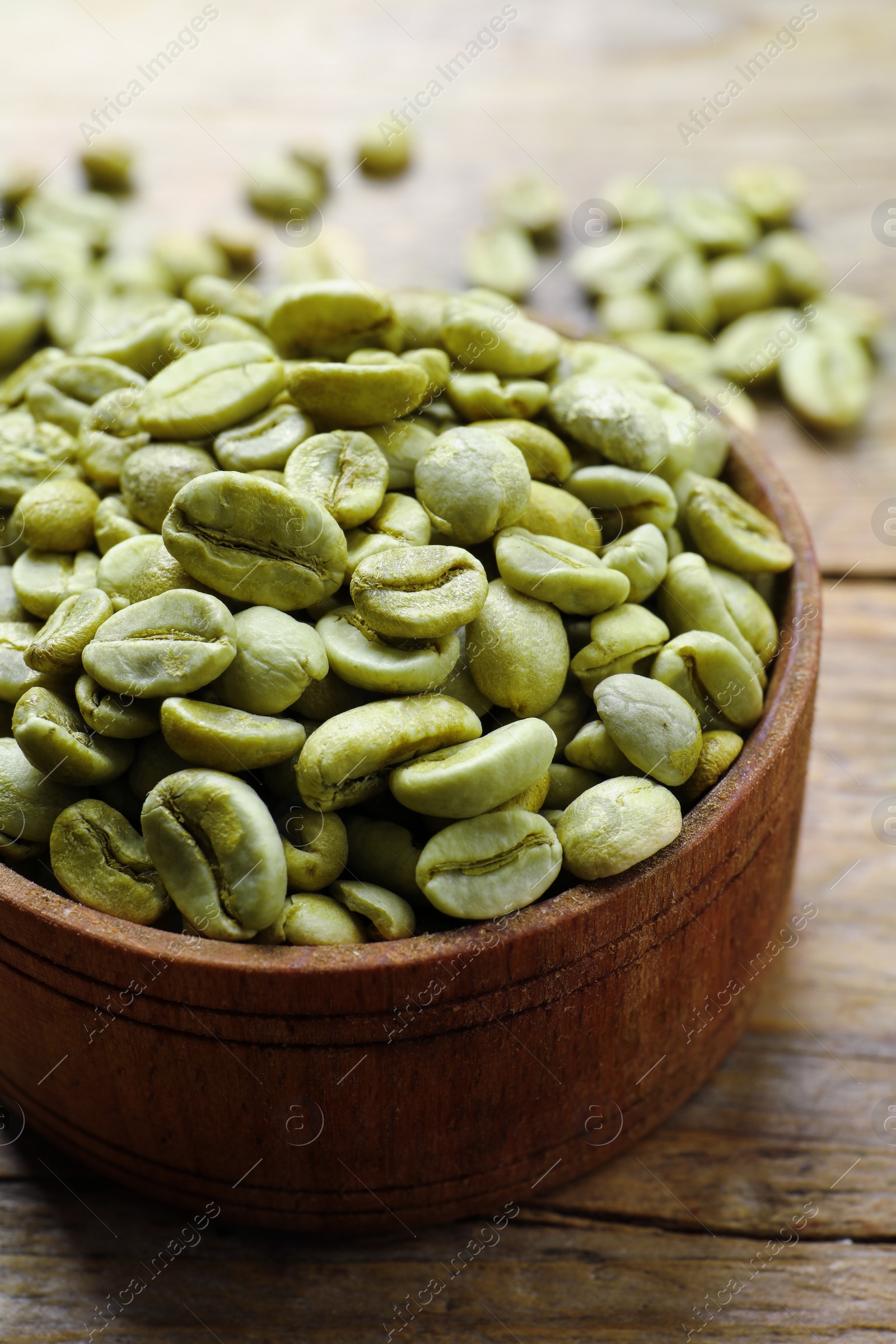 Photo of Green coffee beans in bowl on wooden table, closeup