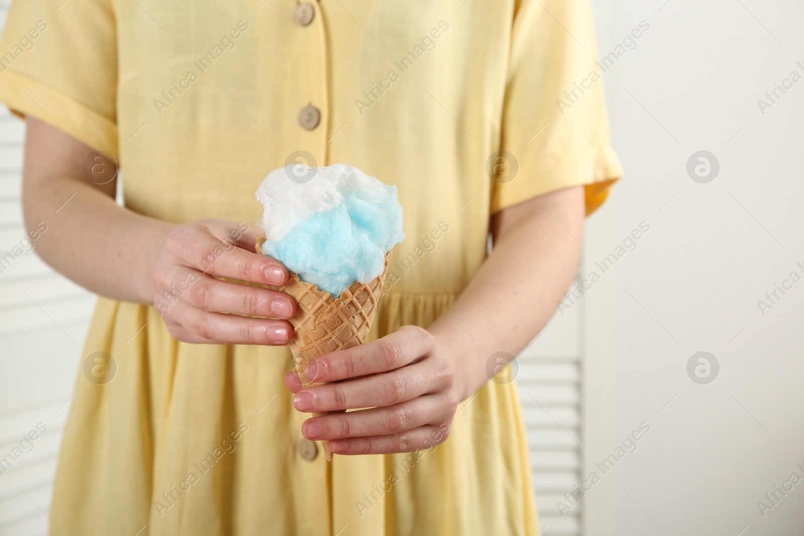 Photo of Woman holding waffle cone with cotton candy indoors, closeup