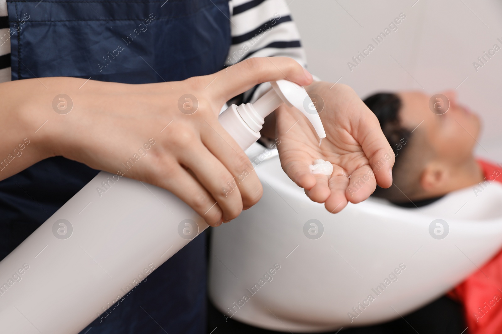 Photo of Professional hairdresser pouring shampoo into hand in salon, closeup