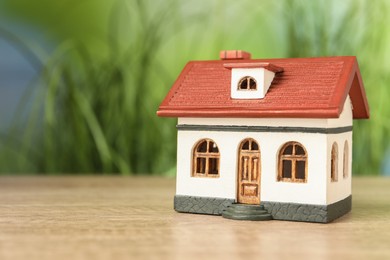 Photo of Mortgage concept. House model on wooden table against blurred green background, space for text