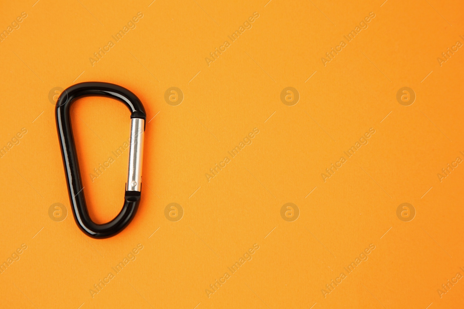 Photo of One black carabiner on orange background, top view. Space for text