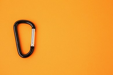 Photo of One black carabiner on orange background, top view. Space for text