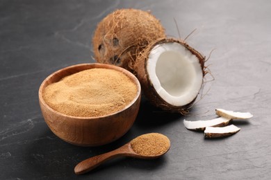 Photo of Spoon with coconut sugar, bowl and fruits on dark textured table, closeup