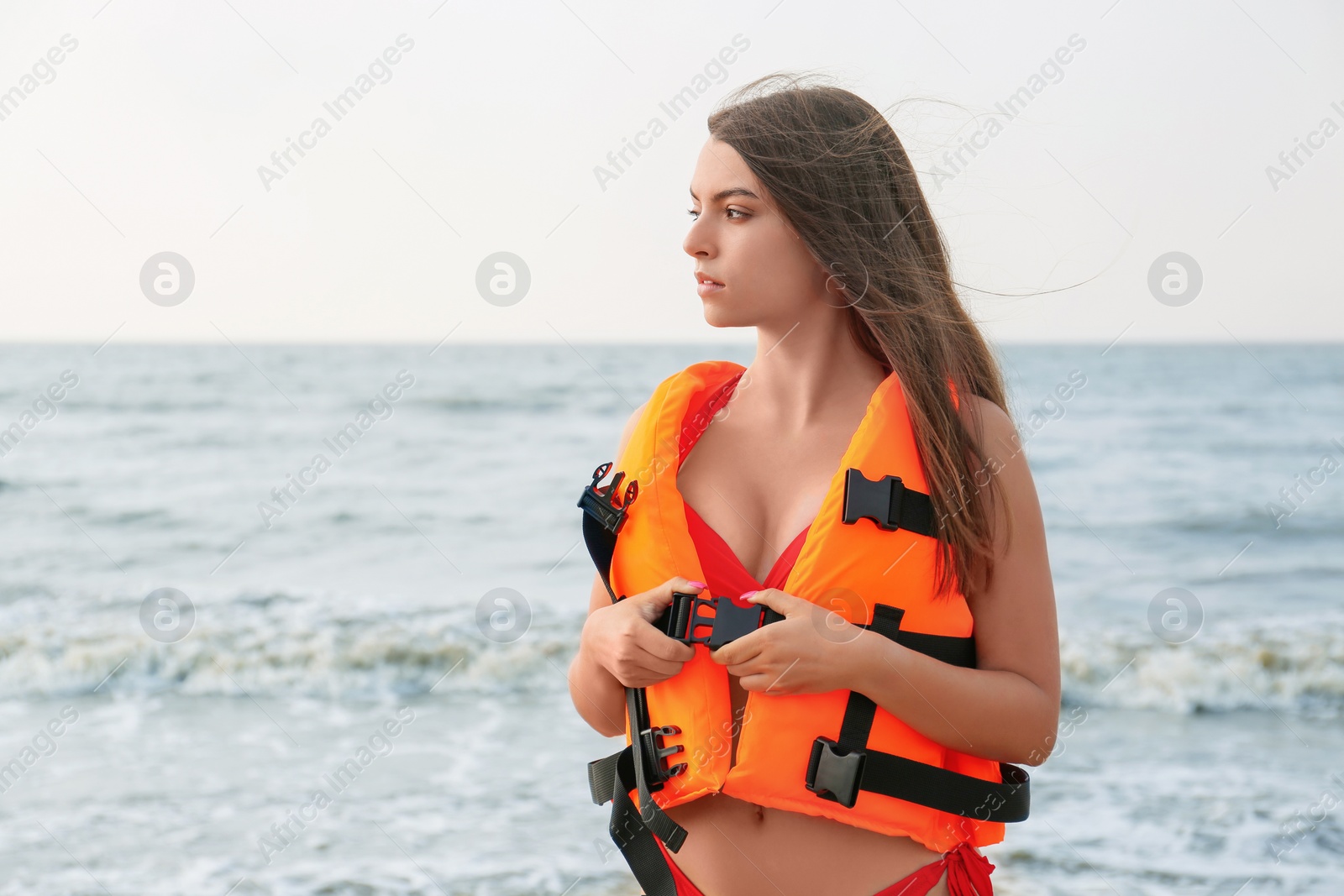 Photo of Beautiful young lifeguard putting on life vest near sea