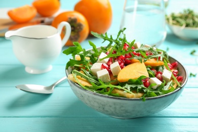 Photo of Delicious persimmon salad with pomegranate and arugula on light blue wooden table