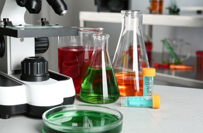 Different glassware with samples and microscope on table in chemistry laboratory