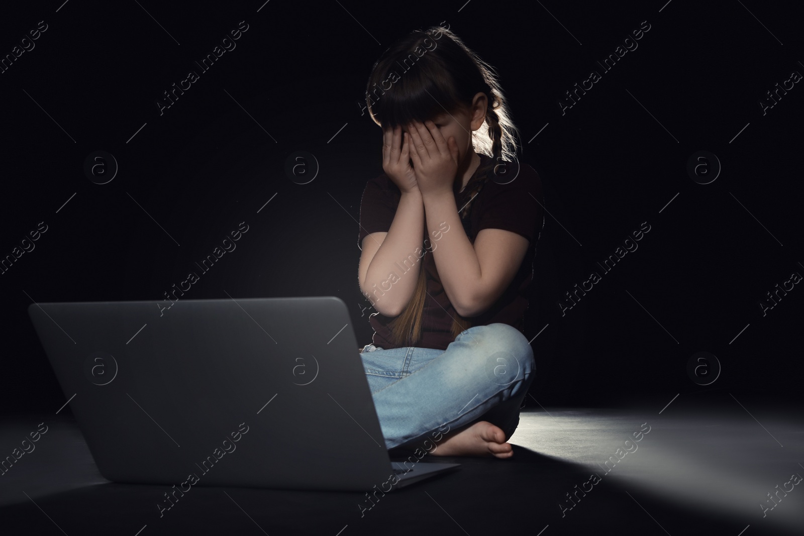 Photo of Frightened little child in front of laptop on dark background. Cyber danger