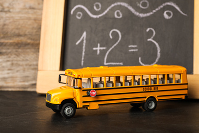 Photo of School bus model on black table near chalkboard. Transport for students