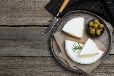 Tasty cut brie cheese with rosemary and olives on wooden table, flat lay. Space for text