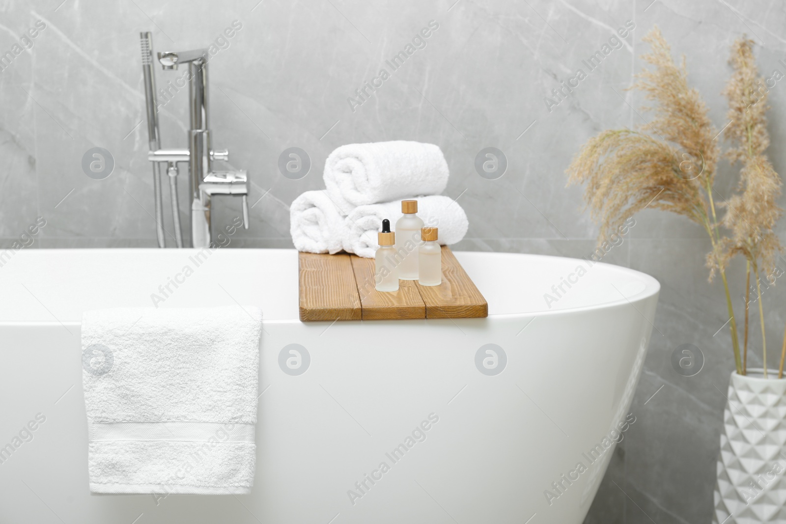 Photo of Rolled bath towels and personal care products on tub tray in bathroom