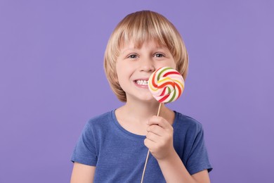 Photo of Happy little boy with colorful lollipop swirl on violet background