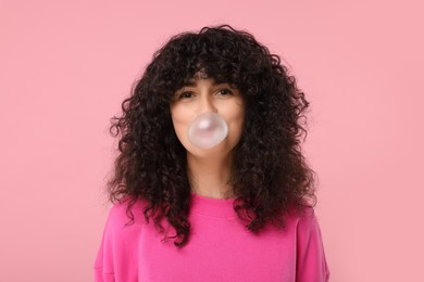 Beautiful young woman blowing bubble gum on pink background