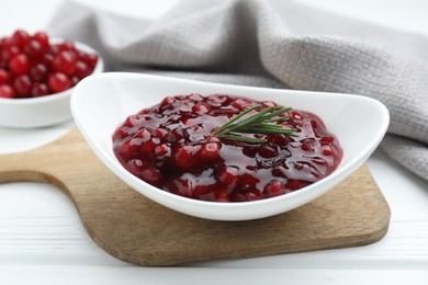 Photo of Fresh cranberry sauce and rosemary in bowl on white wooden table, closeup