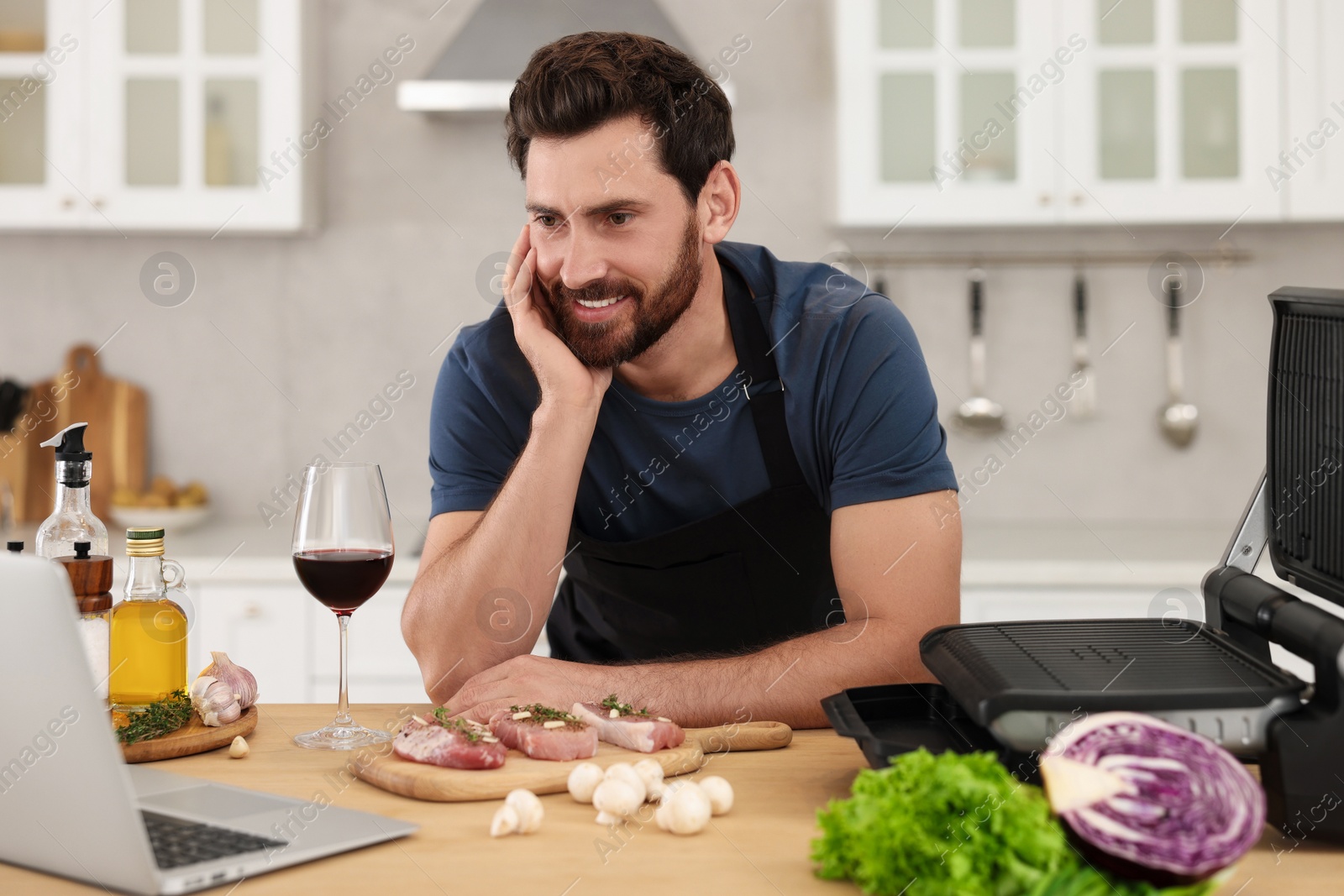 Photo of Man making dinner while watching online cooking course via laptop in kitchen