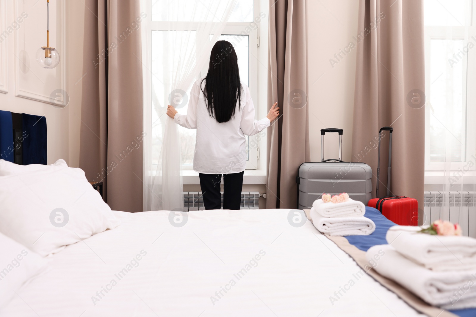 Photo of Businesswoman opening window curtains in hotel room, back view