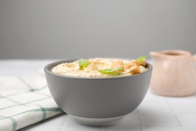 Photo of Delicious hummus with chickpeas served on white tiled table, closeup