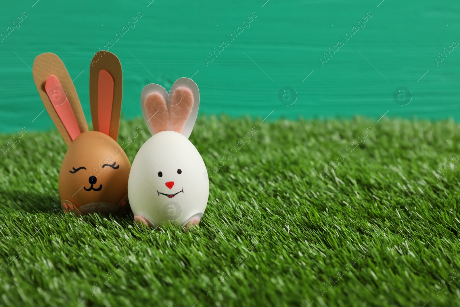 Photo of Easter eggs as cute bunnies on green grass, space for text