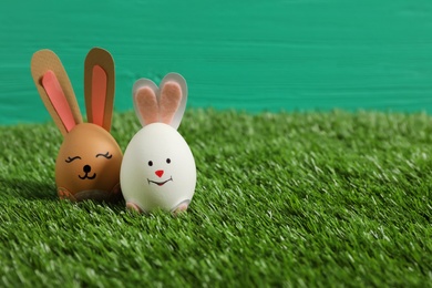 Easter eggs as cute bunnies on green grass, space for text