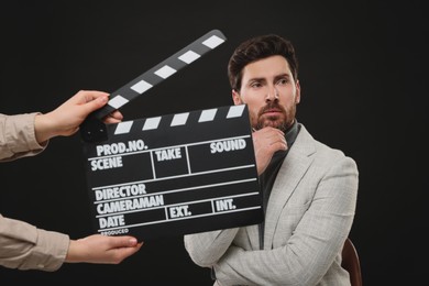 Photo of Actor performing while second assistant camera holding clapperboard on black background