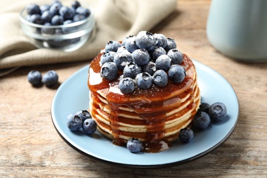 Photo of Delicious pancakes with fresh blueberries and syrup on wooden table