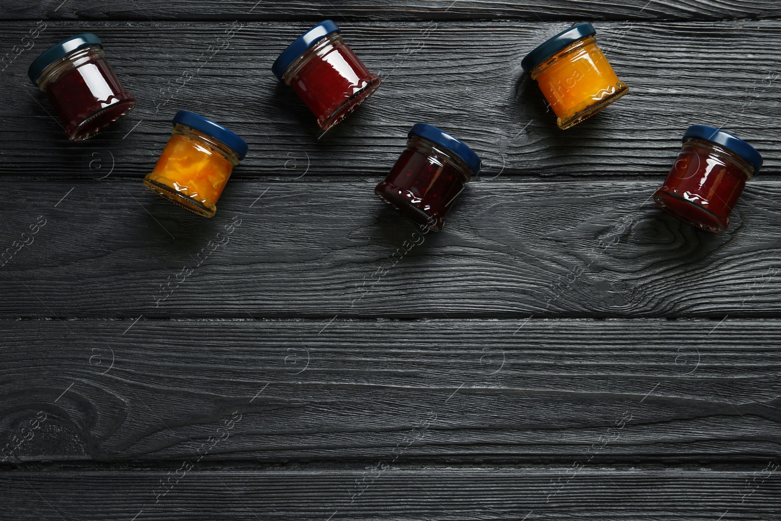 Photo of Jars of different jams on black wooden table, flat lay. Space for text