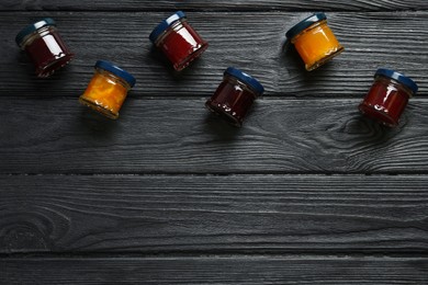 Photo of Jars of different jams on black wooden table, flat lay. Space for text