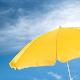 Image of Open big yellow beach umbrella and beautiful blue sky with white clouds on background