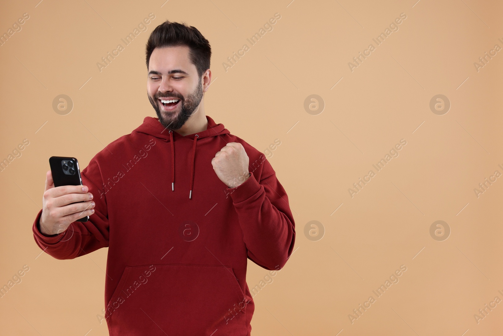 Photo of Happy young man using smartphone on beige background, space for text