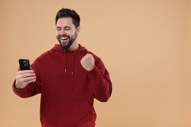 Happy young man using smartphone on beige background, space for text