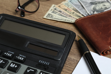 Photo of Calculator, pen and wallet with money on wooden table, closeup. Tax accounting