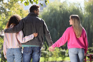 Photo of Man holding hands with another woman while hugging his girlfriend during walk in park, back view. Love triangle