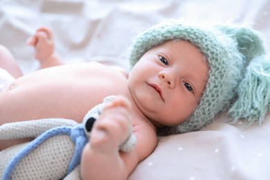 Cute newborn baby in warm hat with toy on bed