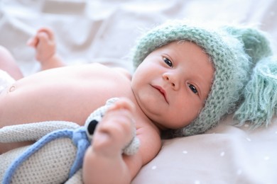 Photo of Cute newborn baby in warm hat with toy on bed