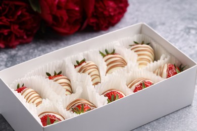 Delicious chocolate covered strawberries in box and flowers on light grey table, closeup