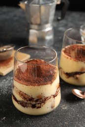 Photo of Delicious tiramisu in glasses on grey textured table