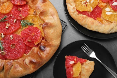 Photo of Tasty galette with citrus fruits served on grey table, flat lay
