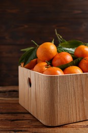 Photo of Fresh tangerines with green leaves in crate on wooden table, closeup