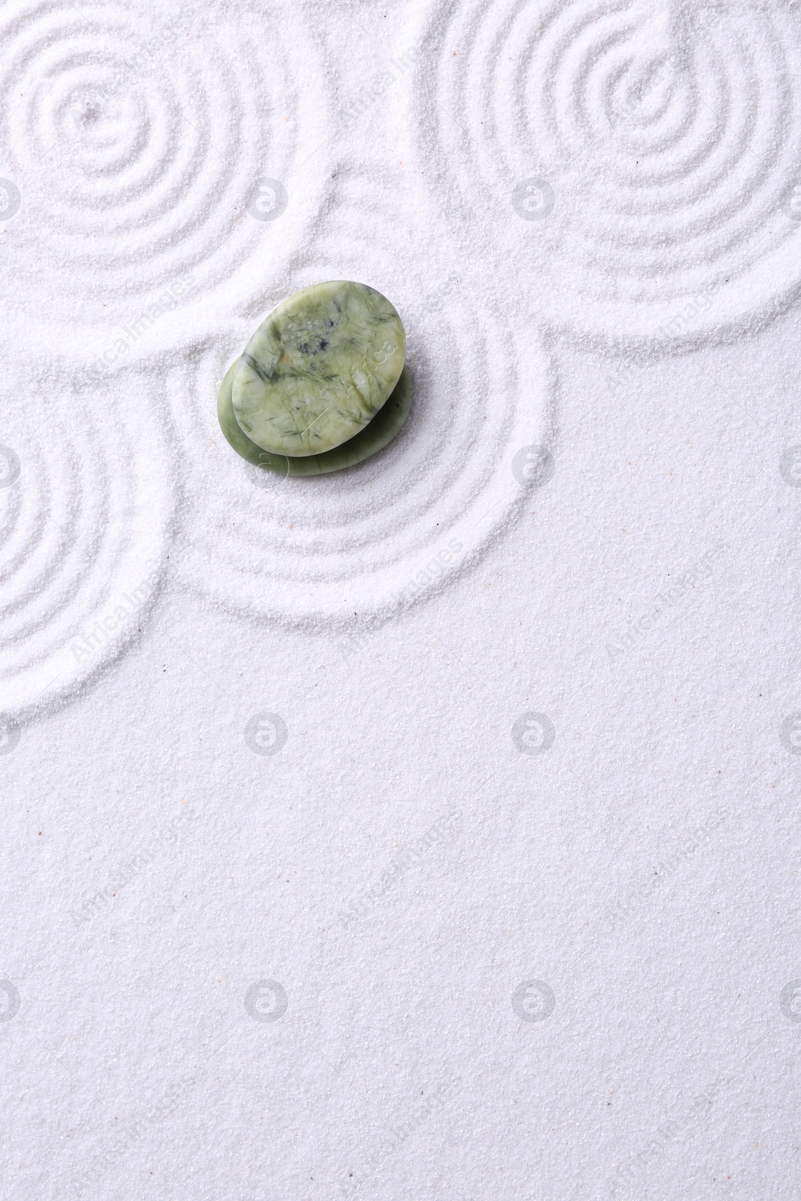 Photo of Zen garden stones on white sand with pattern, top view. Space for text