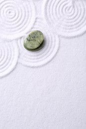 Photo of Zen garden stones on white sand with pattern, top view. Space for text