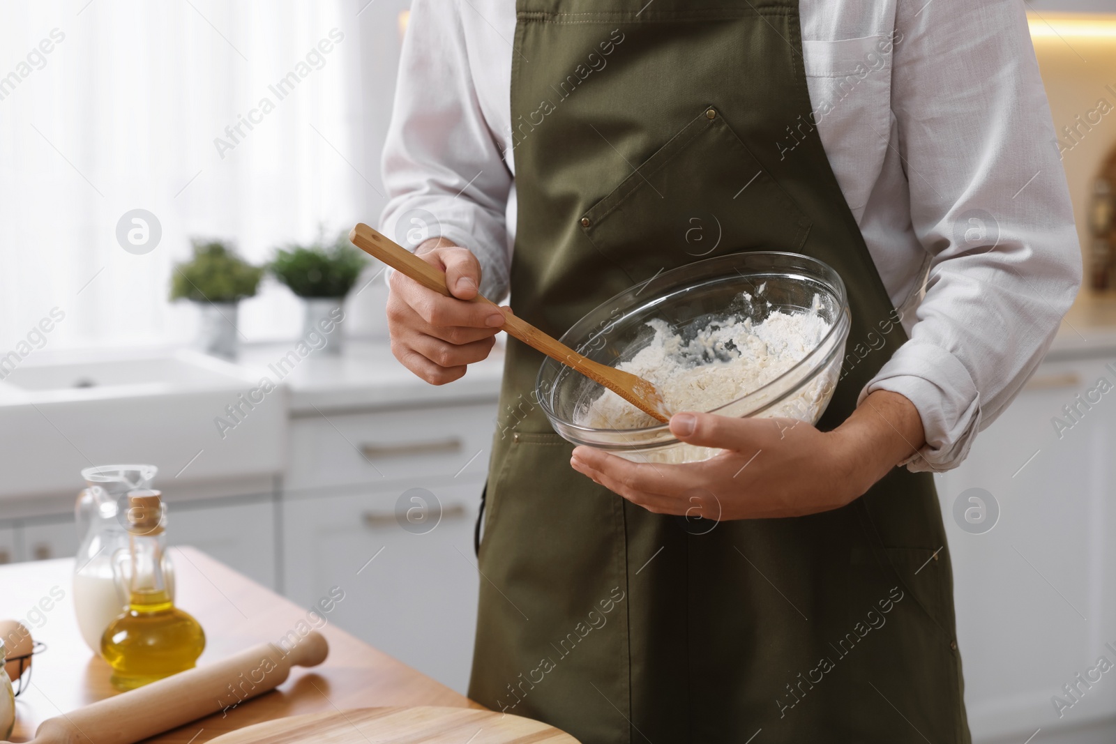 Photo of Making bread. Man preparing dough in bowl at wooden table in kitchen, closeup