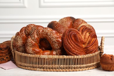 Photo of Wicker basket with different tasty freshly baked pastries on white wooden table, closeup
