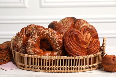 Wicker basket with different tasty freshly baked pastries on white wooden table, closeup